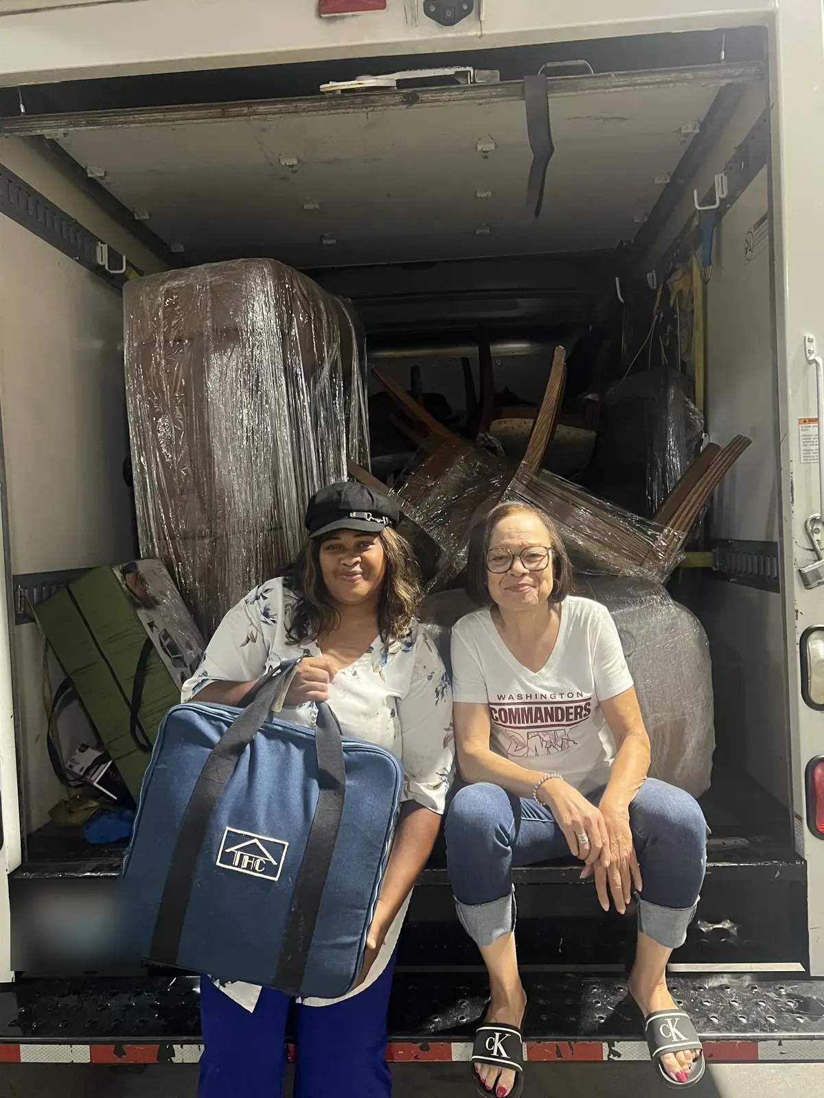 Candis Epps and a donor at the furniture pickup, seated at the back of a truck loaded with donated furniture