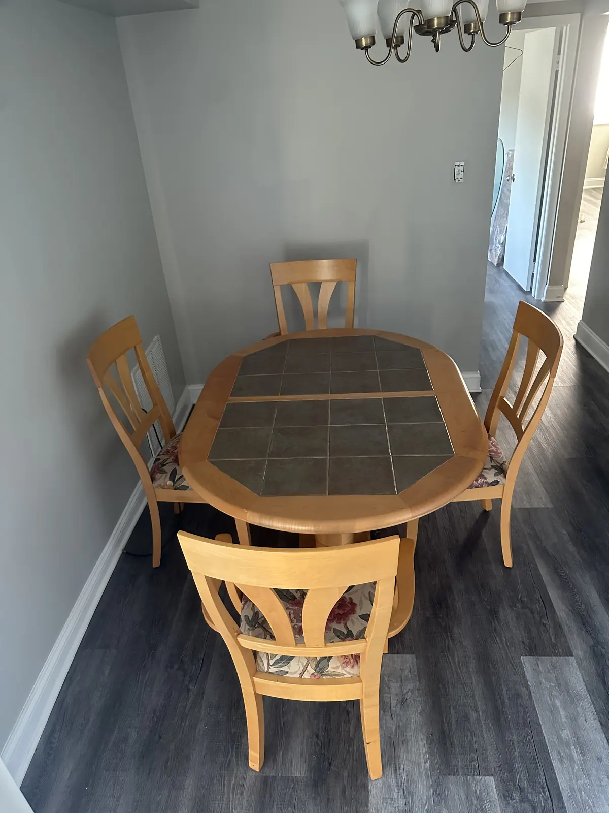 Dinette set with an oval tile-top table and chairs in a dining nook with a chandelier