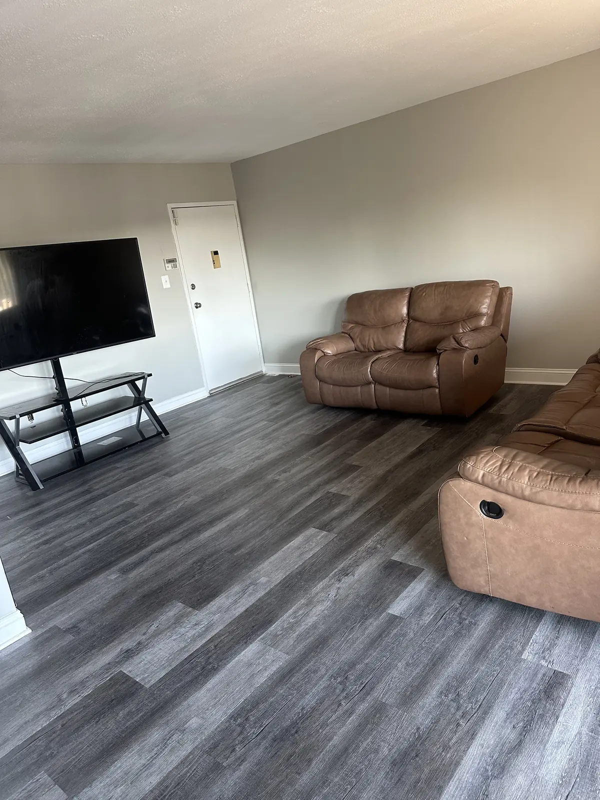 Furnished living room with a brown leather sofa and loveseat, a floor lamp, and a television on a stand