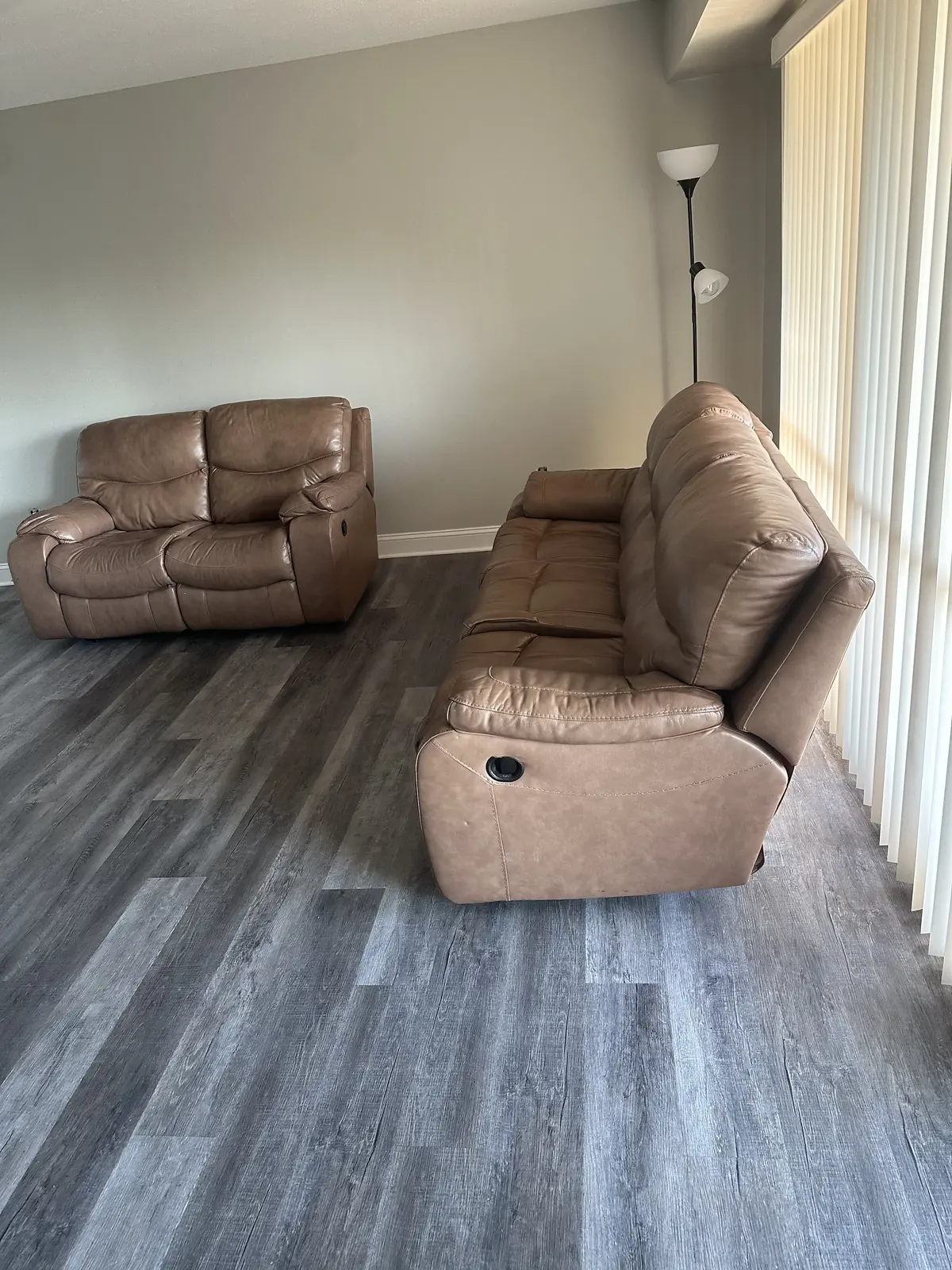 Brown leather loveseat and reclining sofa on new gray plank flooring beside tall windows